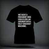 A black short-sleeved t-shirt with white distressed text reading, WE HAVE A PRESIDENT WHO COULD LOSE AN ARGUMENT WITH A SELF-CHECKOUT MACHINE.