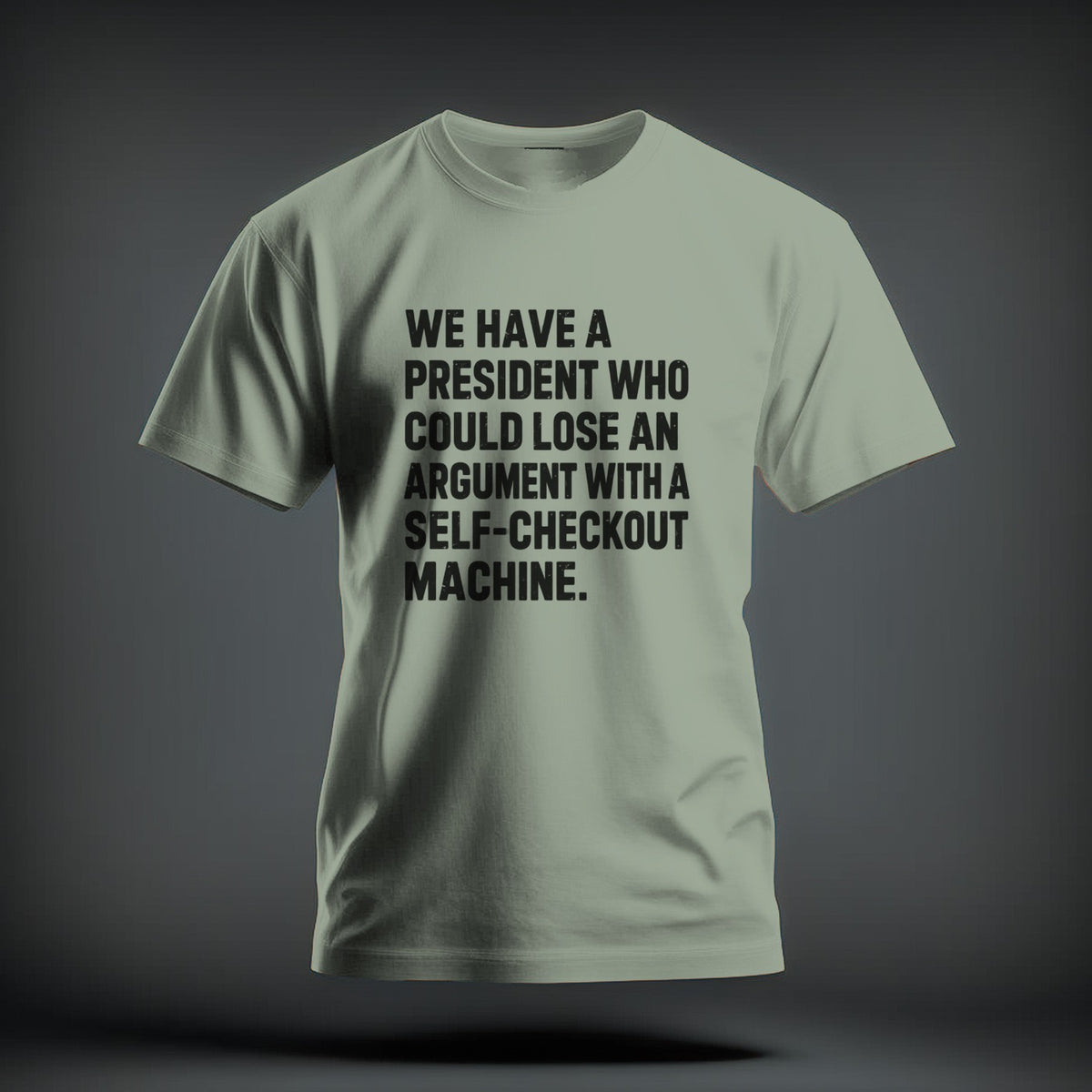 Sage green t-shirt with black text reading "WE HAVE A PRESIDENT WHO COULD LOSE AN ARGUMENT WITH A SELF-CHECKOUT MACHINE."
