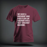 Maroon t-shirt with white distressed text reading WE HAVE A PRESIDENT WHO COULD LOSE AN ARGUMENT WITH A SELF-CHECKOUT MACHINE.