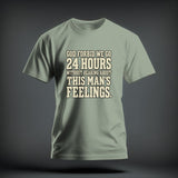 A sage green t-shirt with centered block text reading God Forbid We Go 24 Hours Without Hearing About This Mans Feelings.